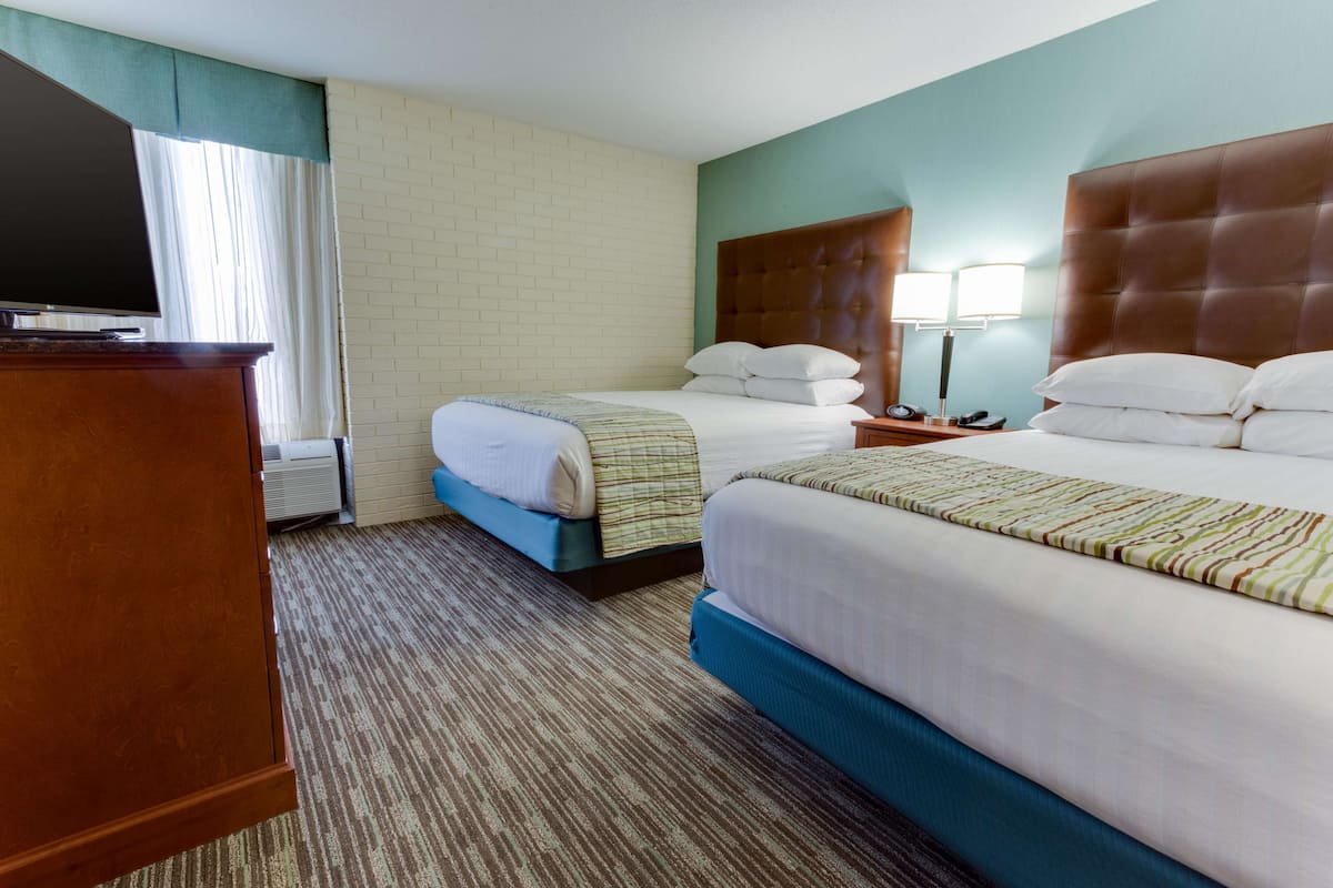 A hotel room with two beds, a television, a desk, and a window with curtains.