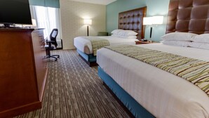 Habitación de hotel con dos camas, un escritorio, un televisor, una silla y una lámpara.