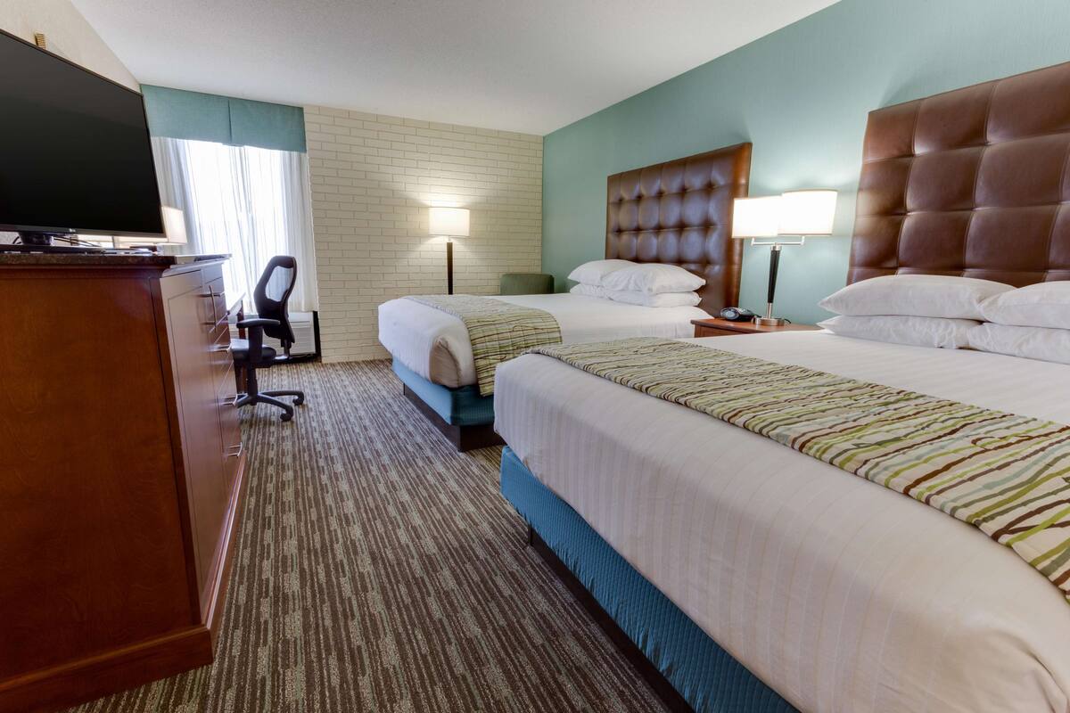 A hotel room with two beds, a desk with a TV, a chair, and a lamp.