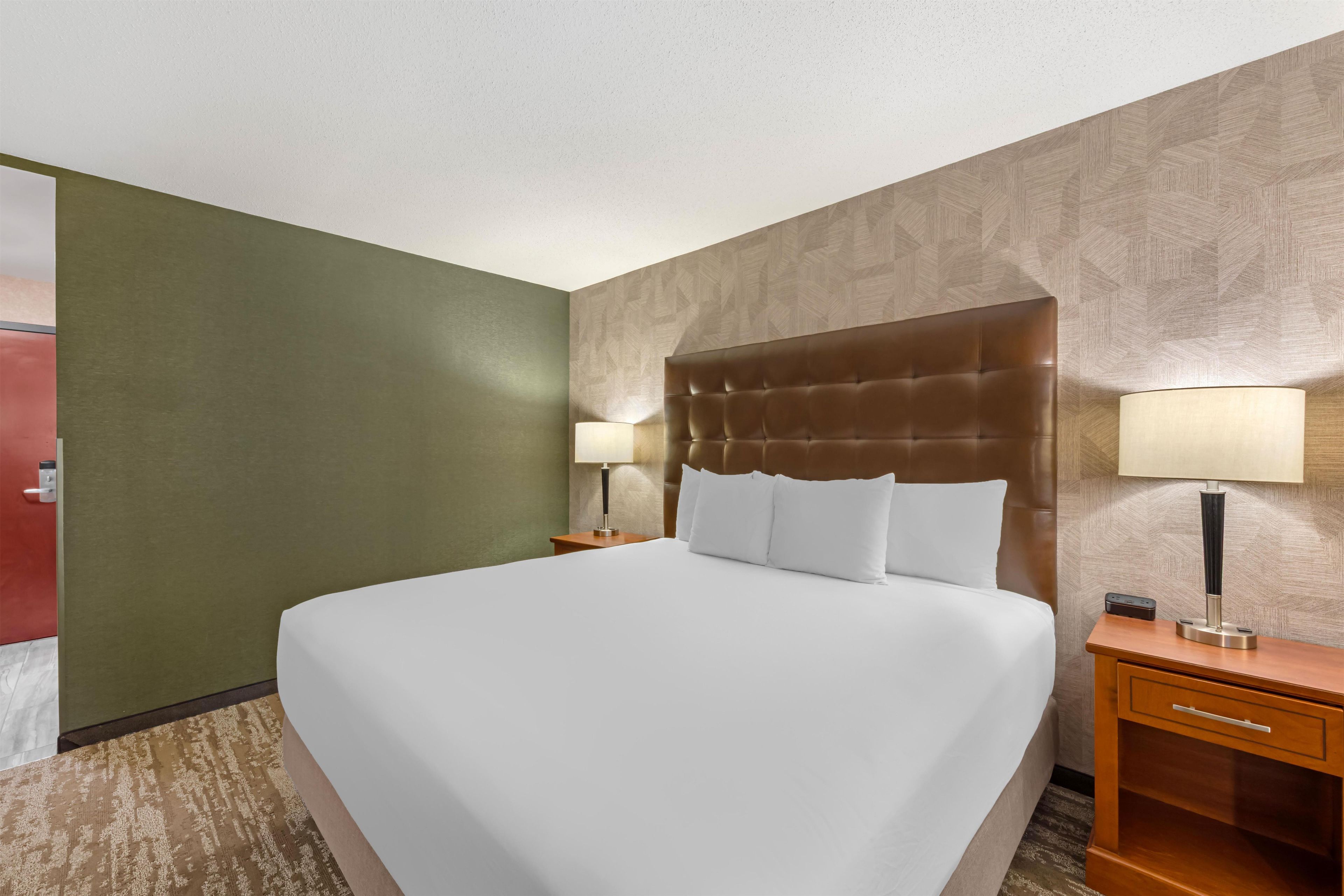 A hotel room with a large bed, two bedside tables, a nightstand, and a wall-mounted lamp.