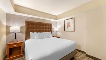 A hotel room with a large bed, two bedside tables with lamps, a wooden nightstand, and a framed picture on the wall.