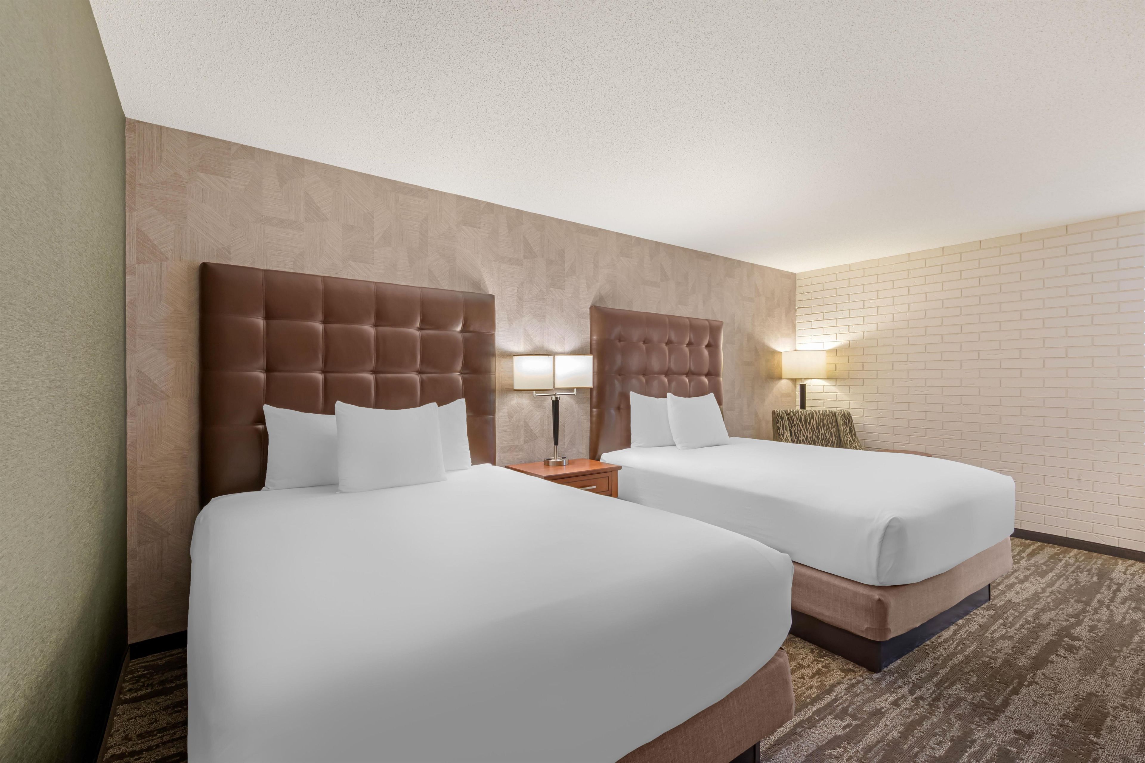 A hotel room with two beds, a brick wall, and a carpeted floor.