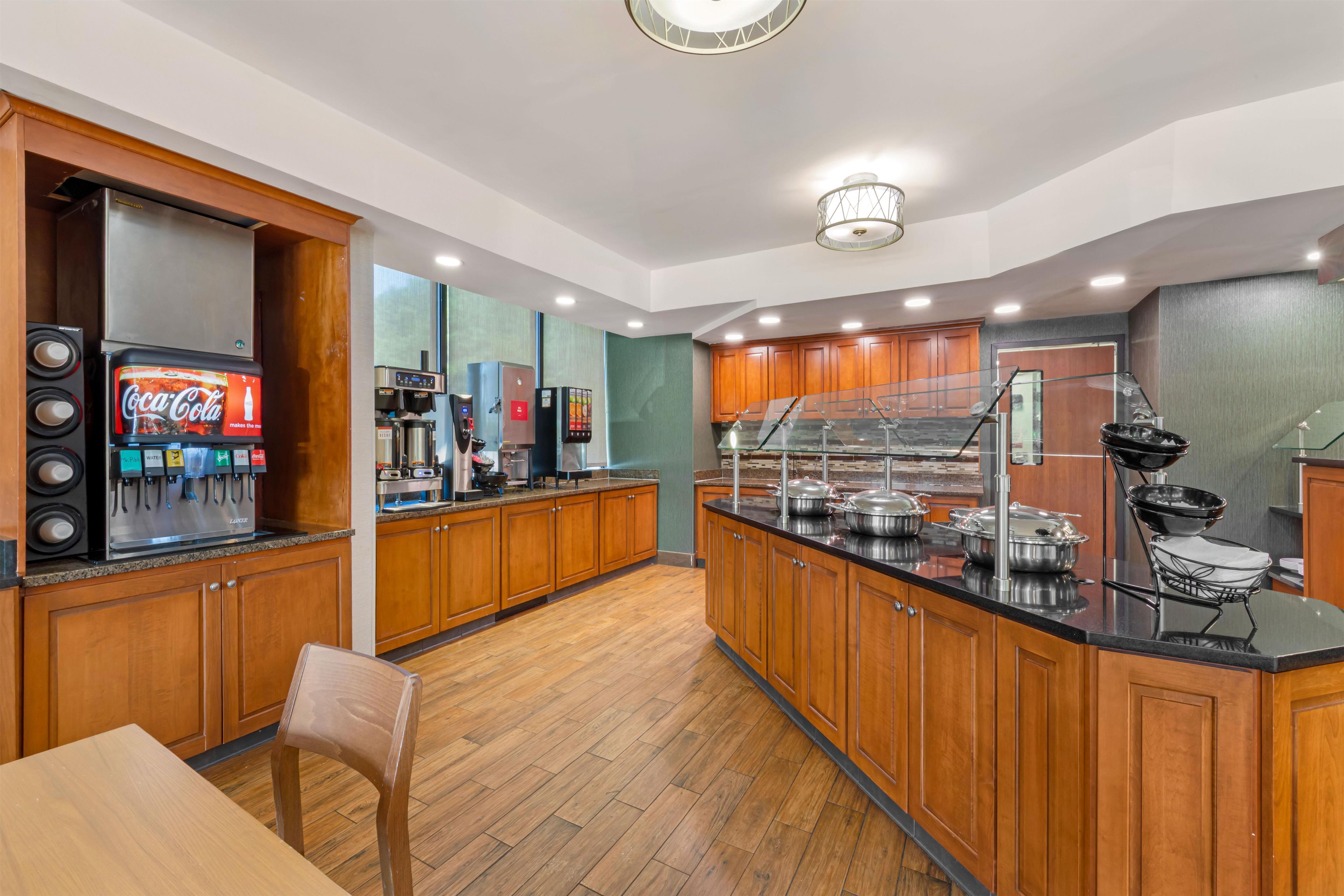 Una cocina moderna con armarios de madera, dispensador de Coca-Cola, cafetera y un espacio tipo bufé.