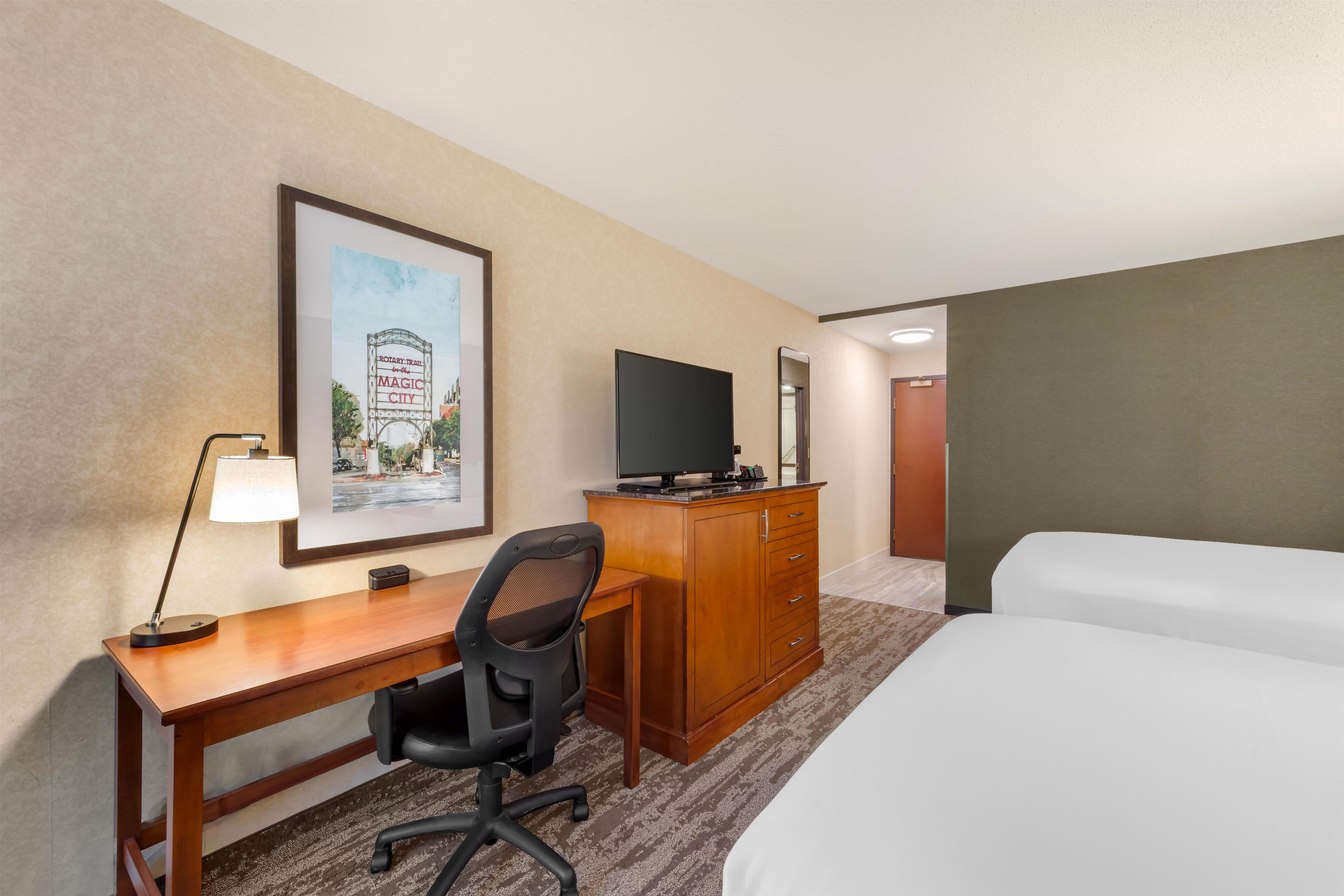 A hotel room with a bed, a desk with a chair, a television, a framed picture on the wall, and a carpeted floor.