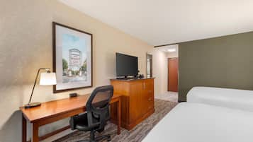 A hotel room with a bed, a desk with a chair, a television, a framed picture on the wall, and a carpeted floor.