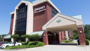 Edificio de Drury Inn & Suites con una entrada destacada, amplias ventanas y un estacionamiento con varios automóviles.
