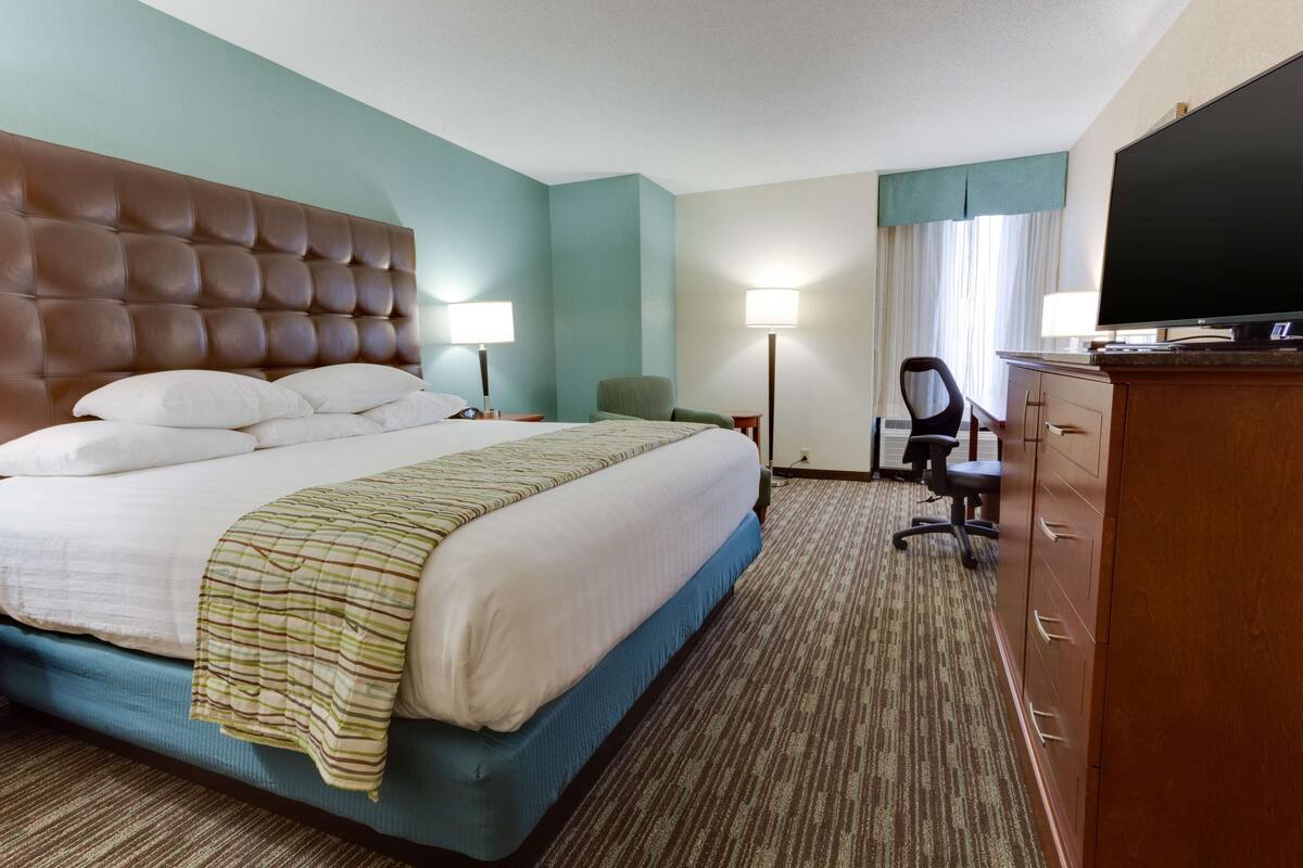 A hotel room with a large bed, two bedside tables, a desk with a chair, a television, and a wardrobe.
