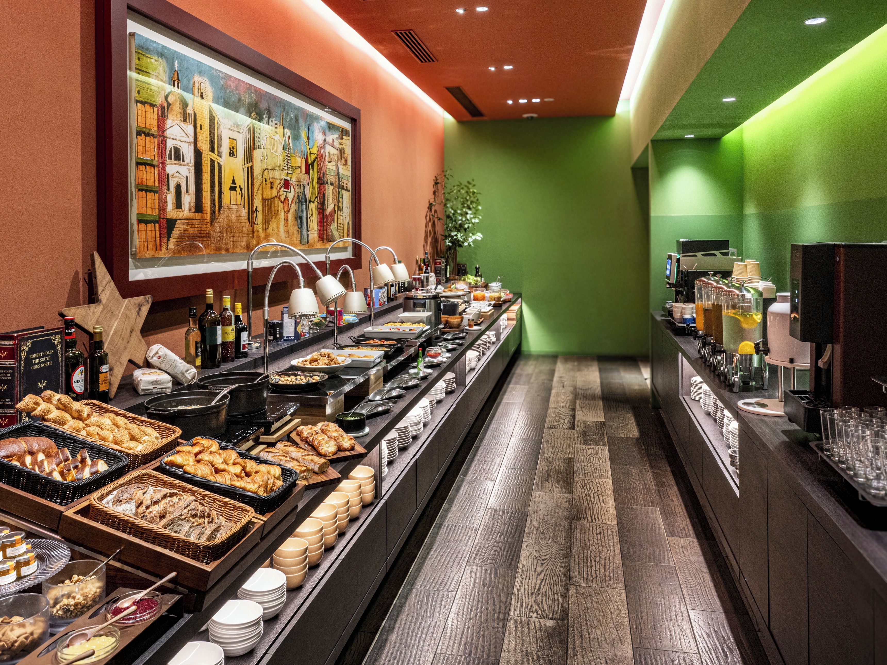 A buffet setup with various food items and beverages, a painting on the wall, and a green accent wall.