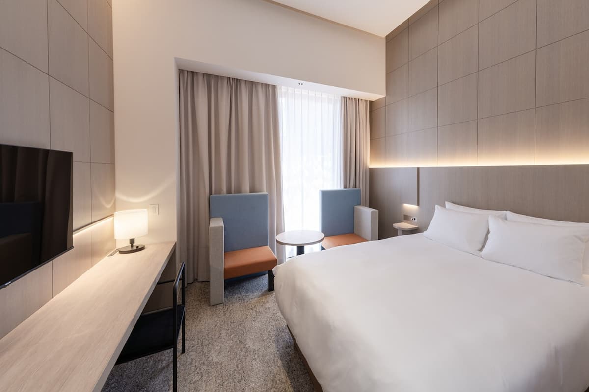 Een moderne hotelkamer met een groot bed, een bureau, twee fauteuils, een kleine tafel en een televisie.