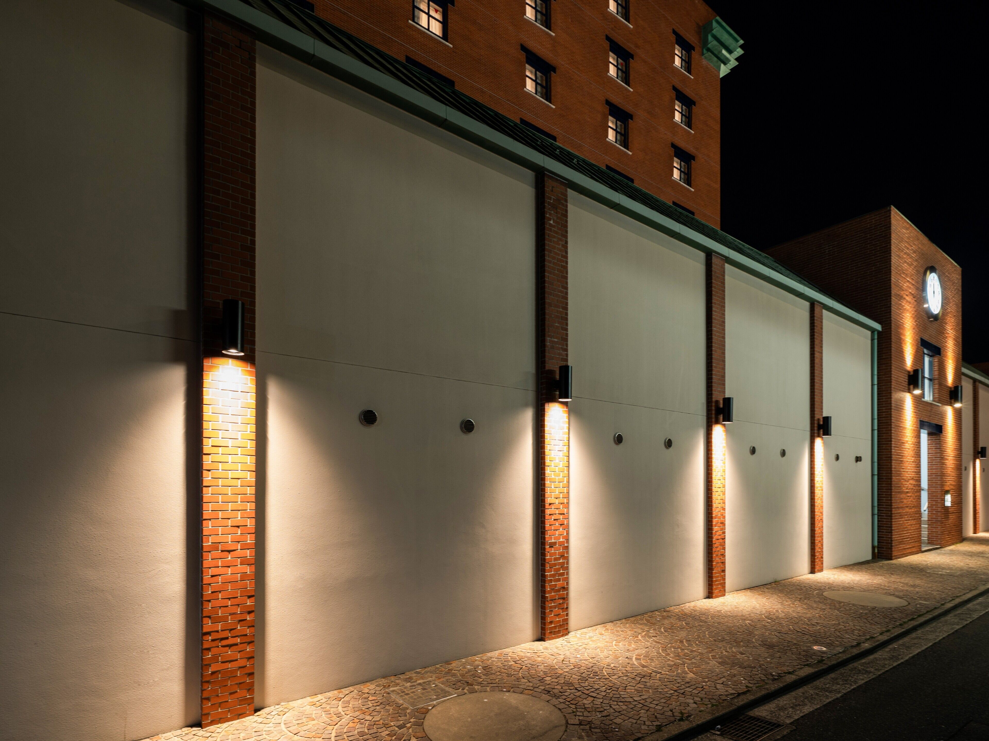 A building with large garage doors, brick walls, and exterior lighting.