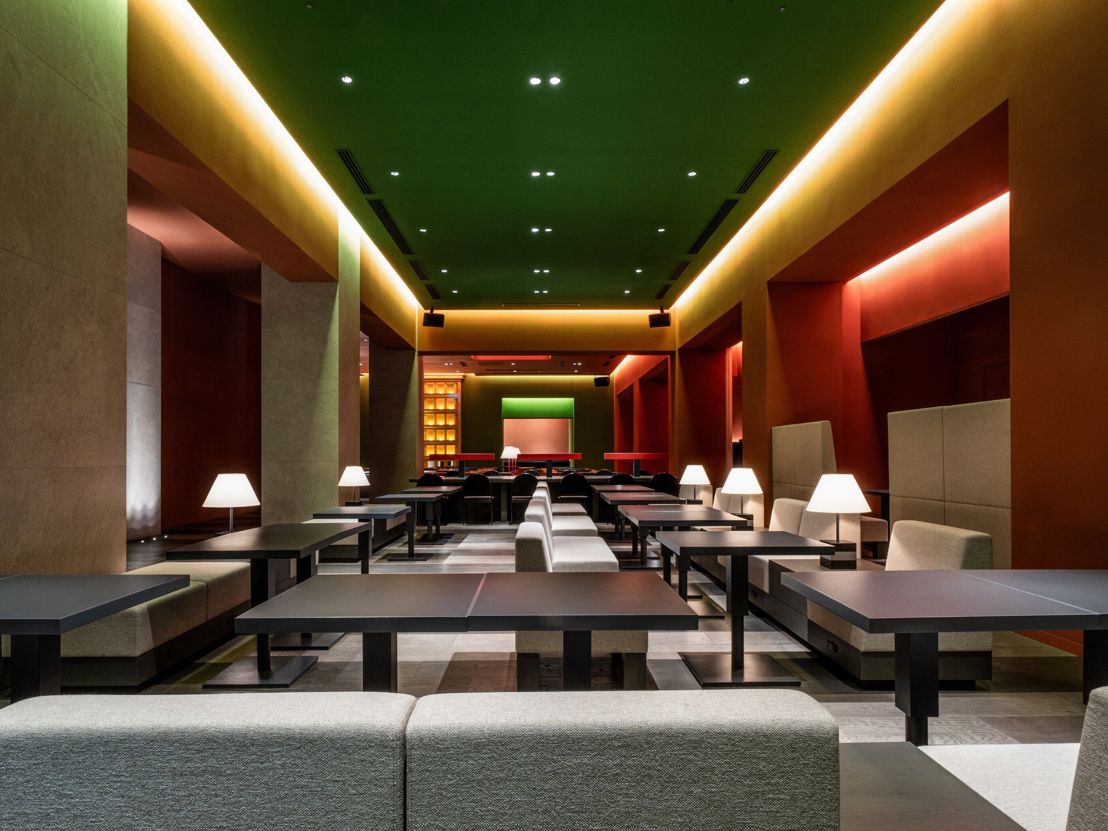 Een moderne hotellobby met een lange receptiebalie, meerdere zithoeken en een groene accentmuur.