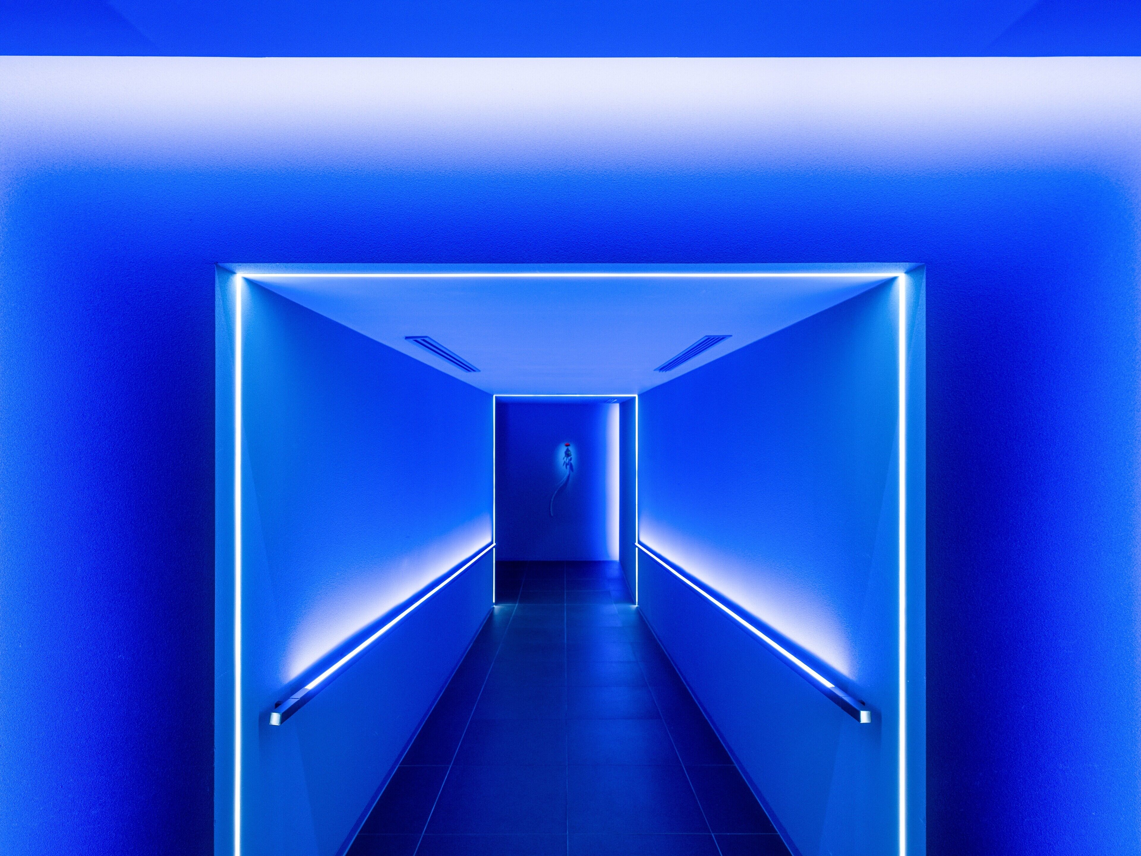 A corridor with blue lighting and a person in the distance.