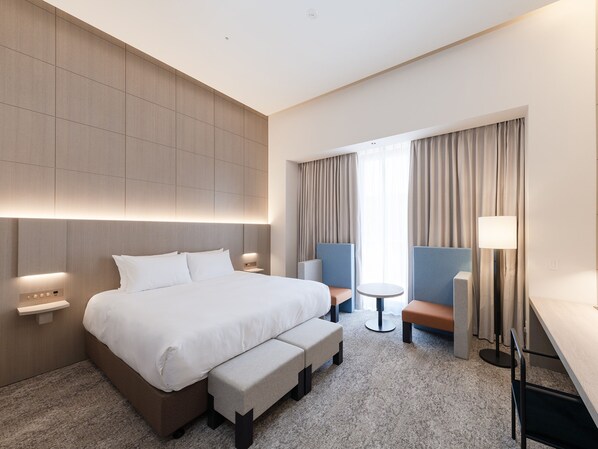 Een moderne hotelkamer met een groot bed, een bureau, een stoel en een klein tafeltje.