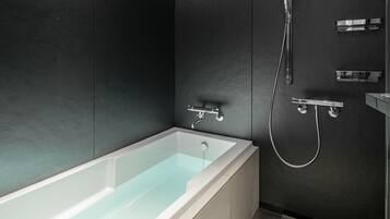 A modern bathroom with a white bathtub, a shower, and a chrome faucet.