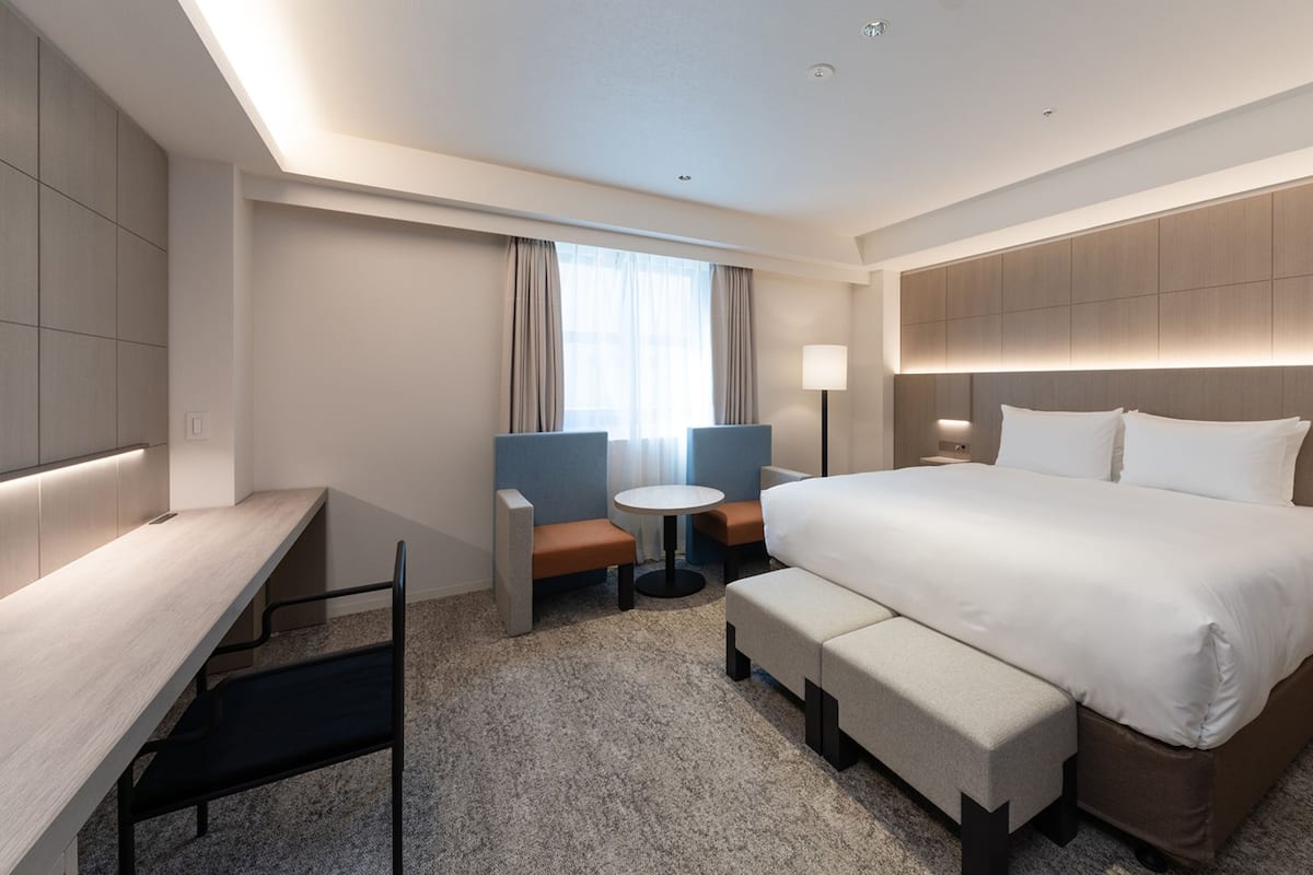 Een moderne hotelkamer met een groot bed, een bureau, een stoel, een bijzettafeltje en een bank.