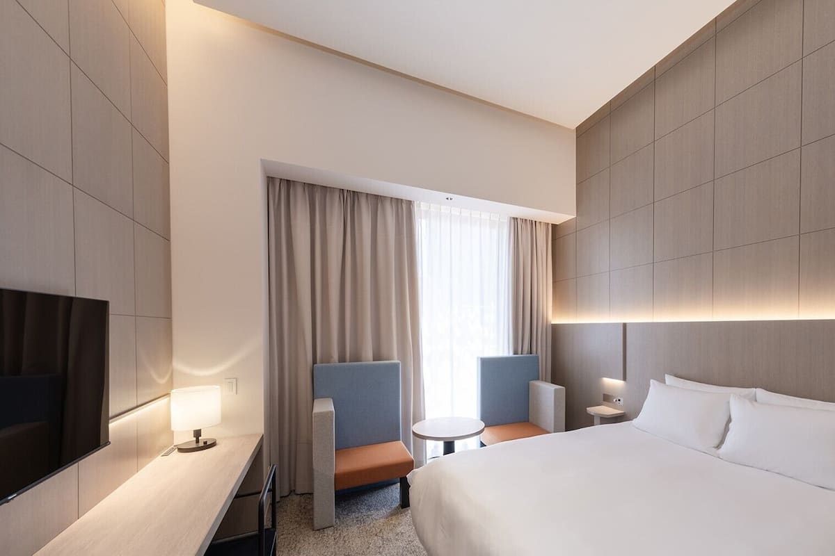 Een moderne hotelkamer met een groot bed, een bureau, een stoel, een klein tafeltje en een televisie.