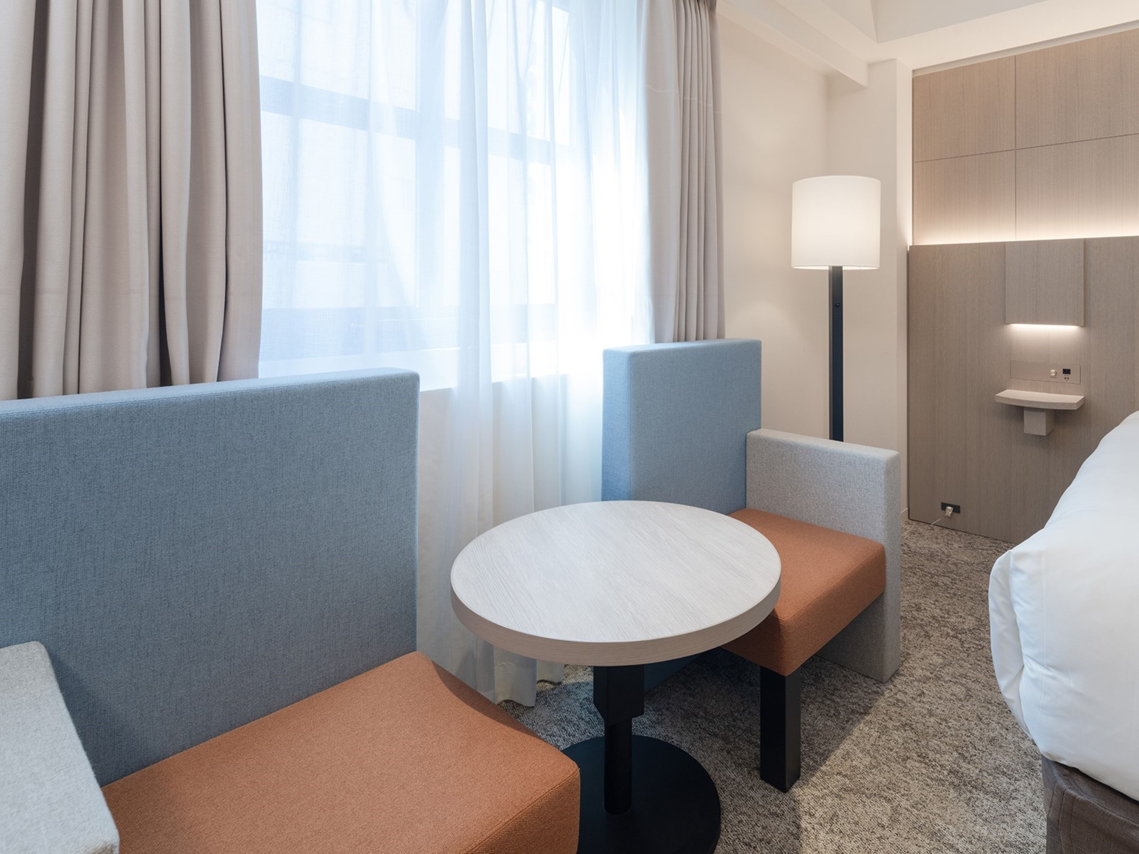 A hotel room with a round table, two sofas, a lamp, and a bedside table.