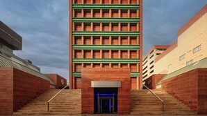 Un edificio moderno con fachada de ladrillo, vigas horizontales verdes y una entrada azul.