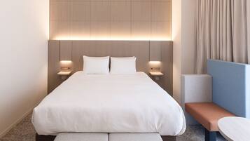 A modern hotel room with a large bed, bedside tables, a bench, and a small table.