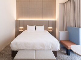 A modern hotel room with a large bed, bedside tables, a bench, and a small table.