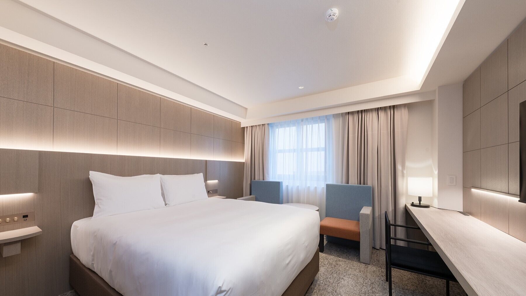 A modern hotel room with a large bed, bedside tables, a desk, and a chair.