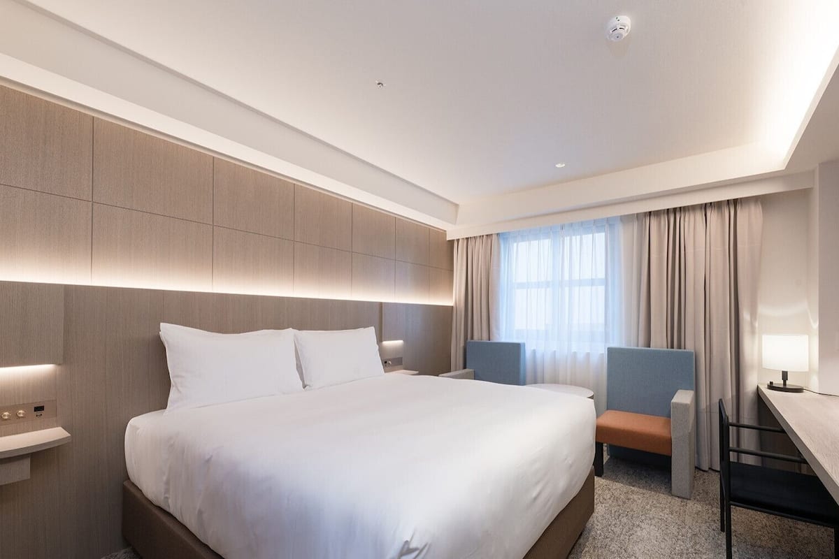 Een moderne hotelkamer met een groot bed, nachtkastjes, een bureau en een stoel.