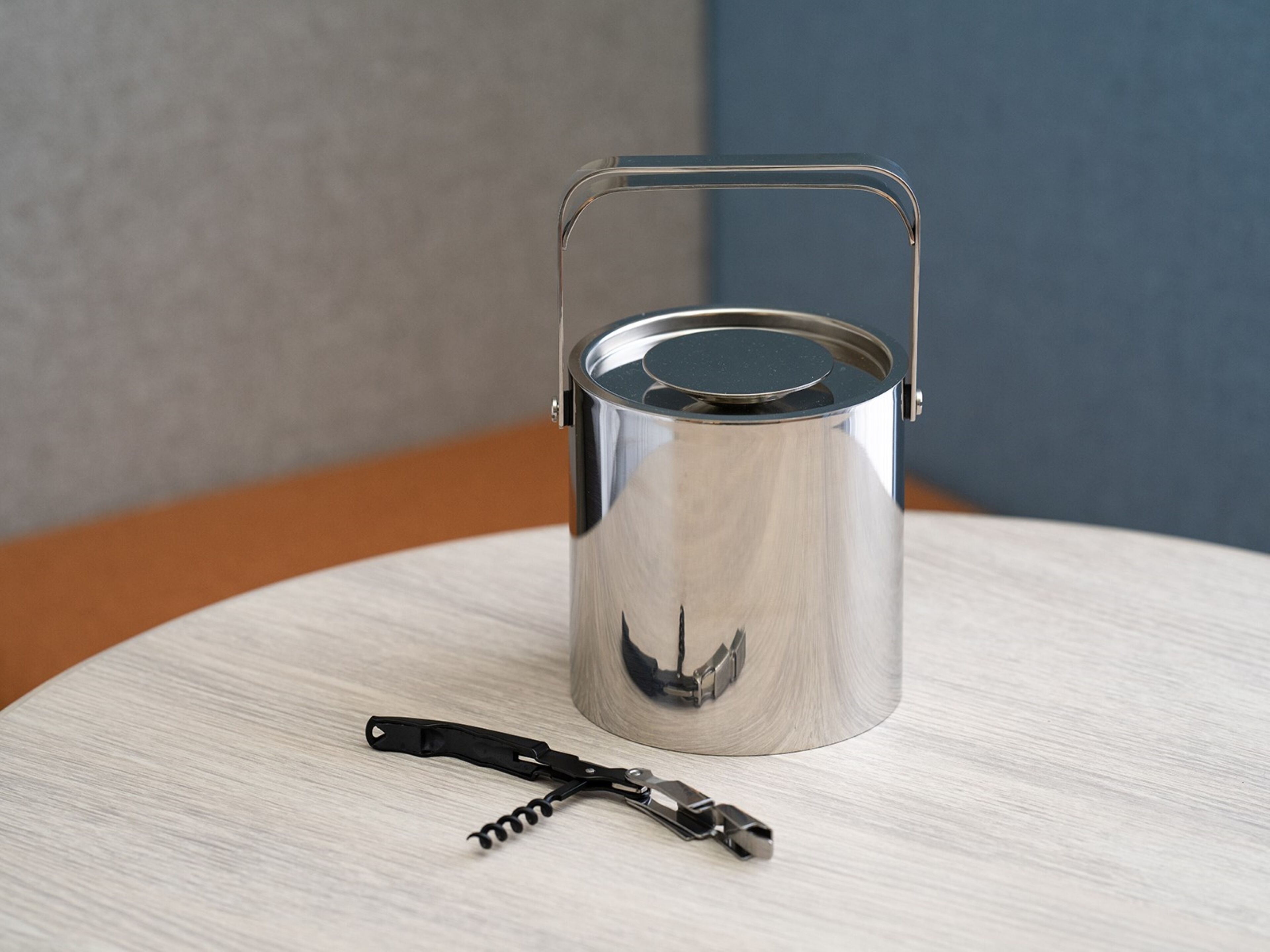 A metallic container with a lid and handle on a round table.