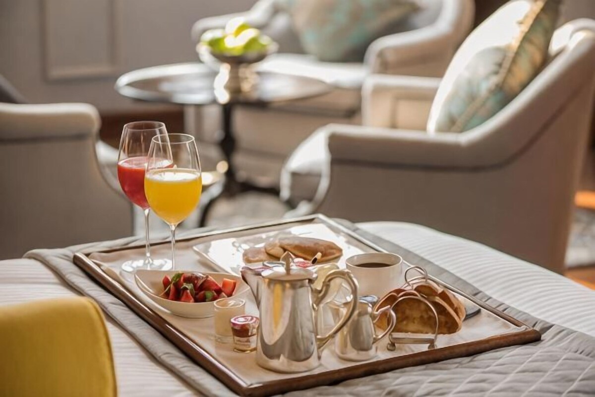 A breakfast tray with a pitcher, cups, and glasses on a tray, set on a bed.