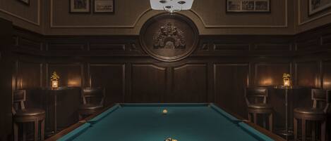 A pool table with balls arranged in a triangle, surrounded by bar stools and framed pictures on the walls.