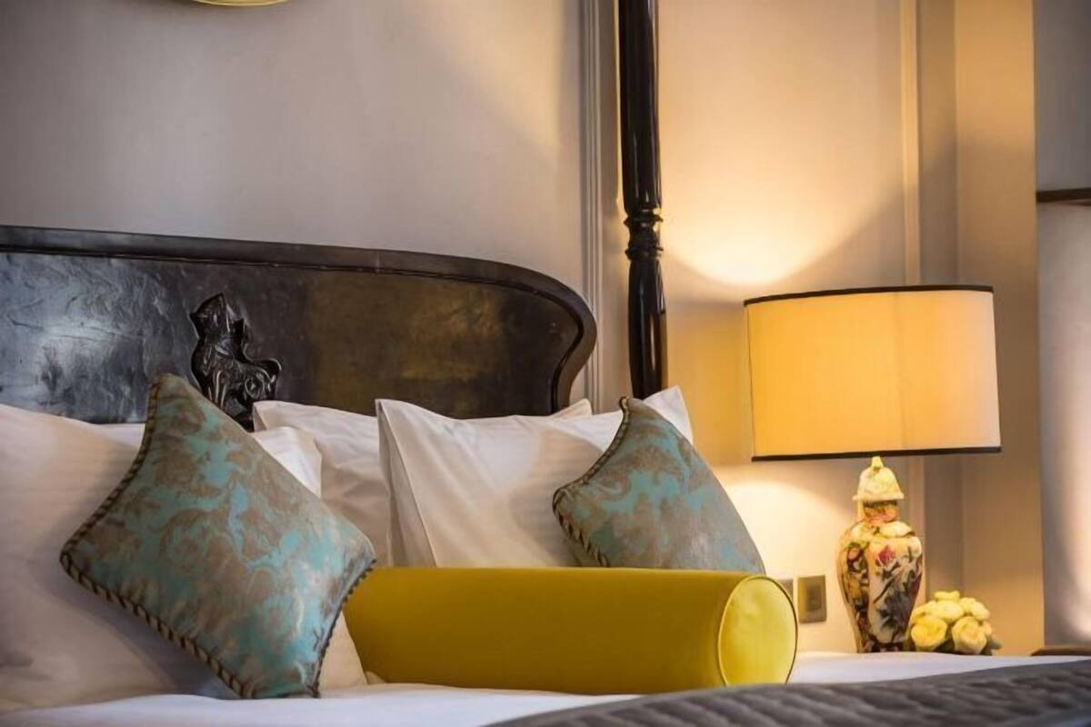 A neatly made bed with white linens and decorative pillows, a bedside lamp, and a yellow accent pillow.