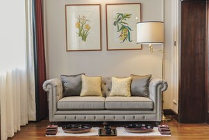 A living room with a grey sofa, two framed botanical prints, a floor lamp, and a small table with bowls and a teapot.