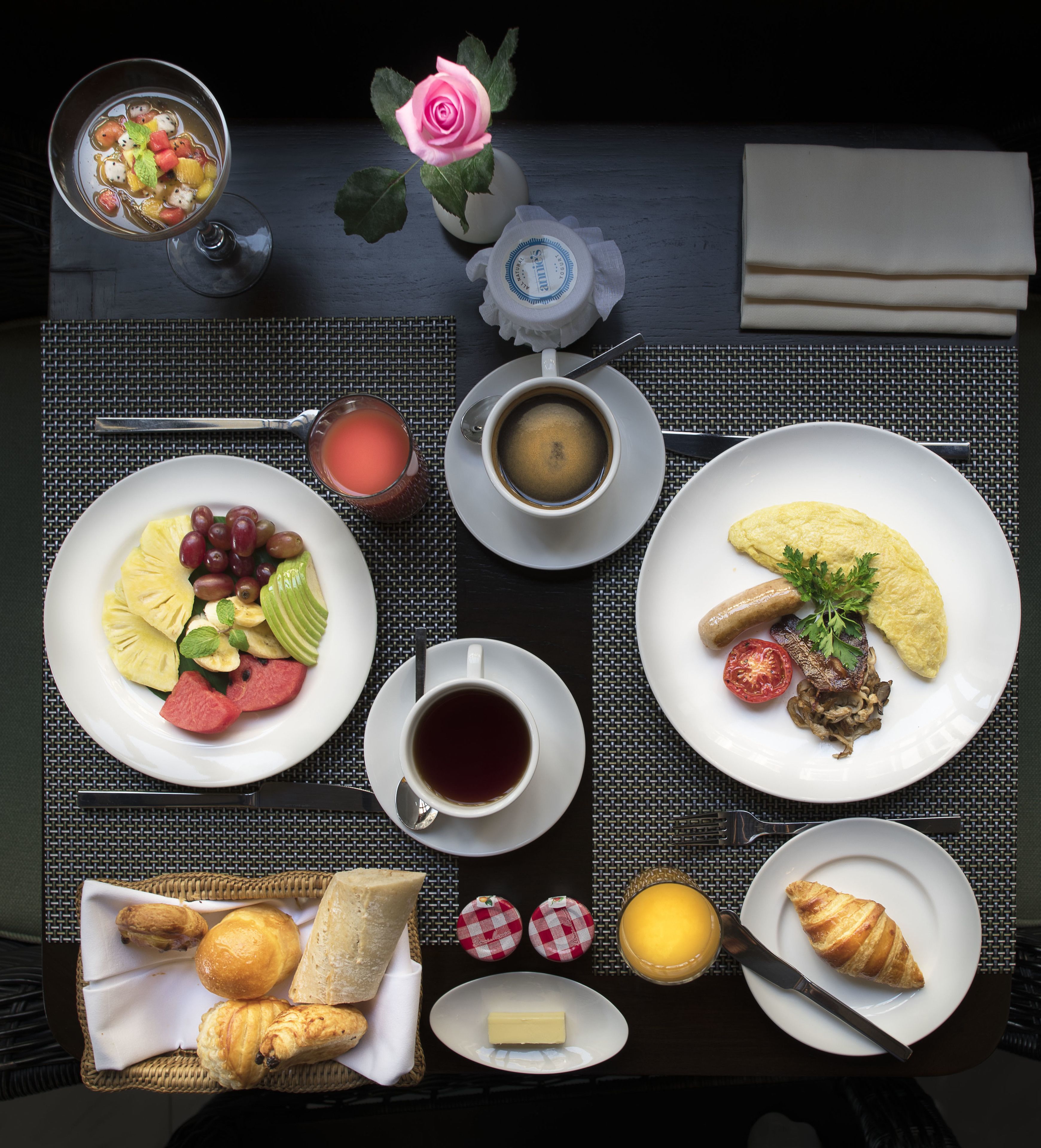 A breakfast setting with plates of fruit, coffee, croissants, and a pastry on a table.
