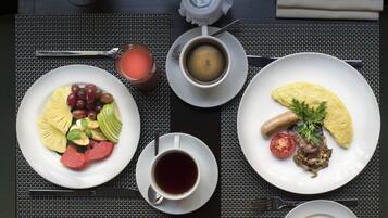 A breakfast setting with plates of fruit, coffee, croissants, and a pastry on a table.