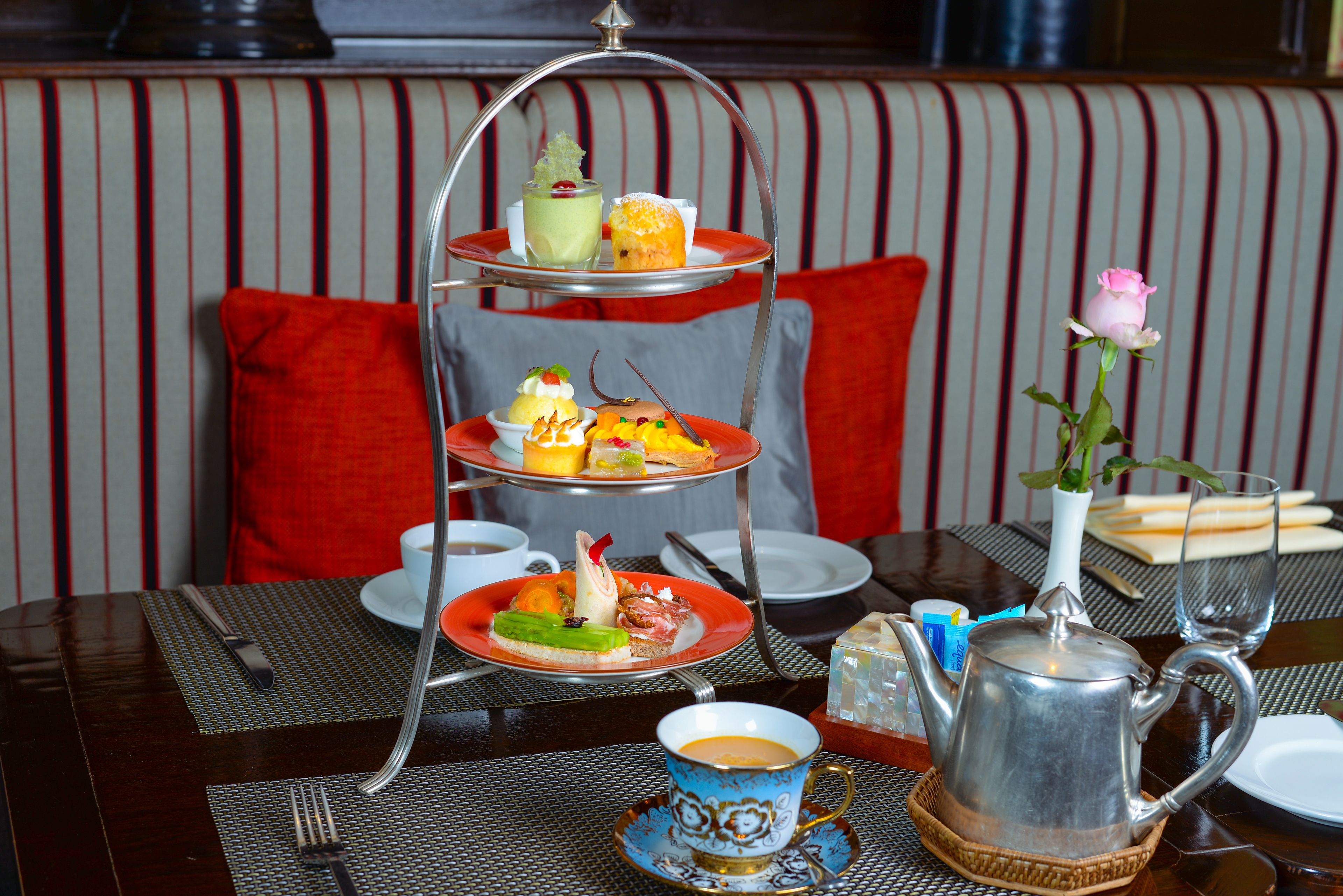 A three-tiered dessert stand with various pastries and a cup of coffee on a table.