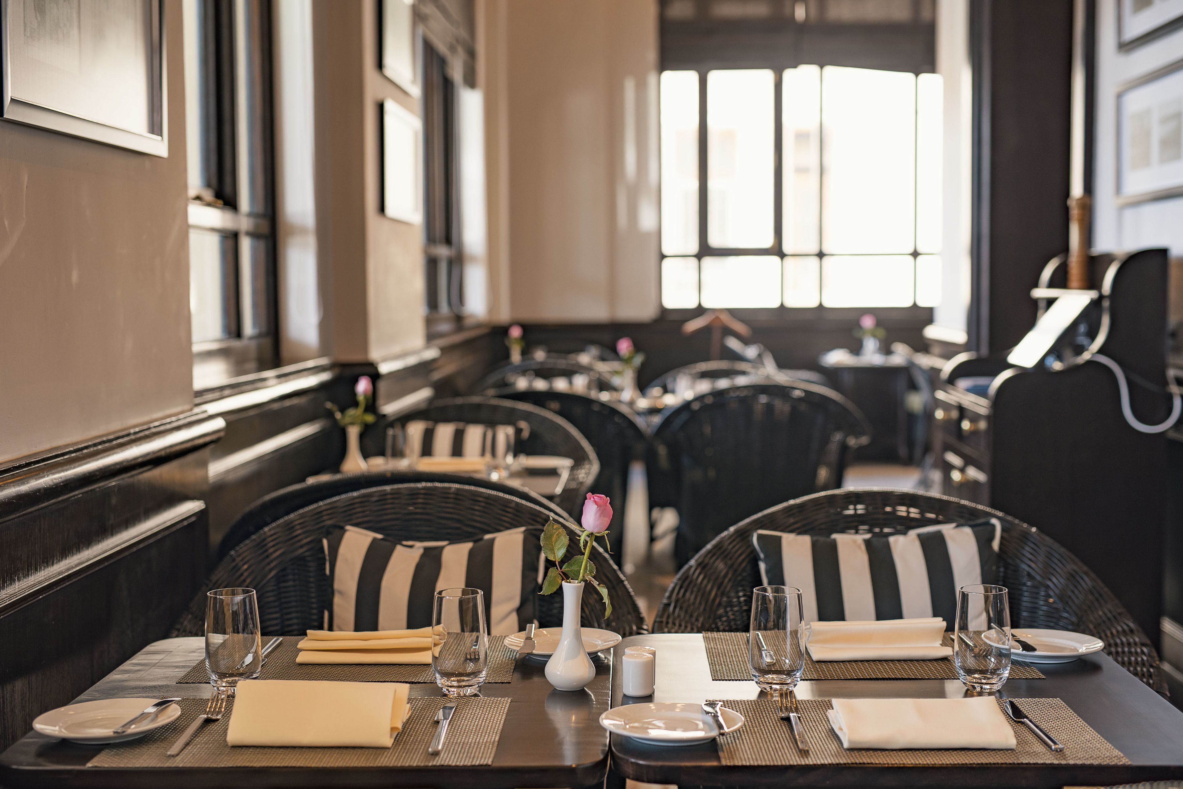 A restaurant with wicker chairs, black and white striped cushions, and a vase with a single rose.
