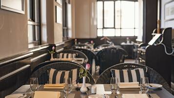 A restaurant with wicker chairs, black and white striped cushions, and a vase with a single rose.