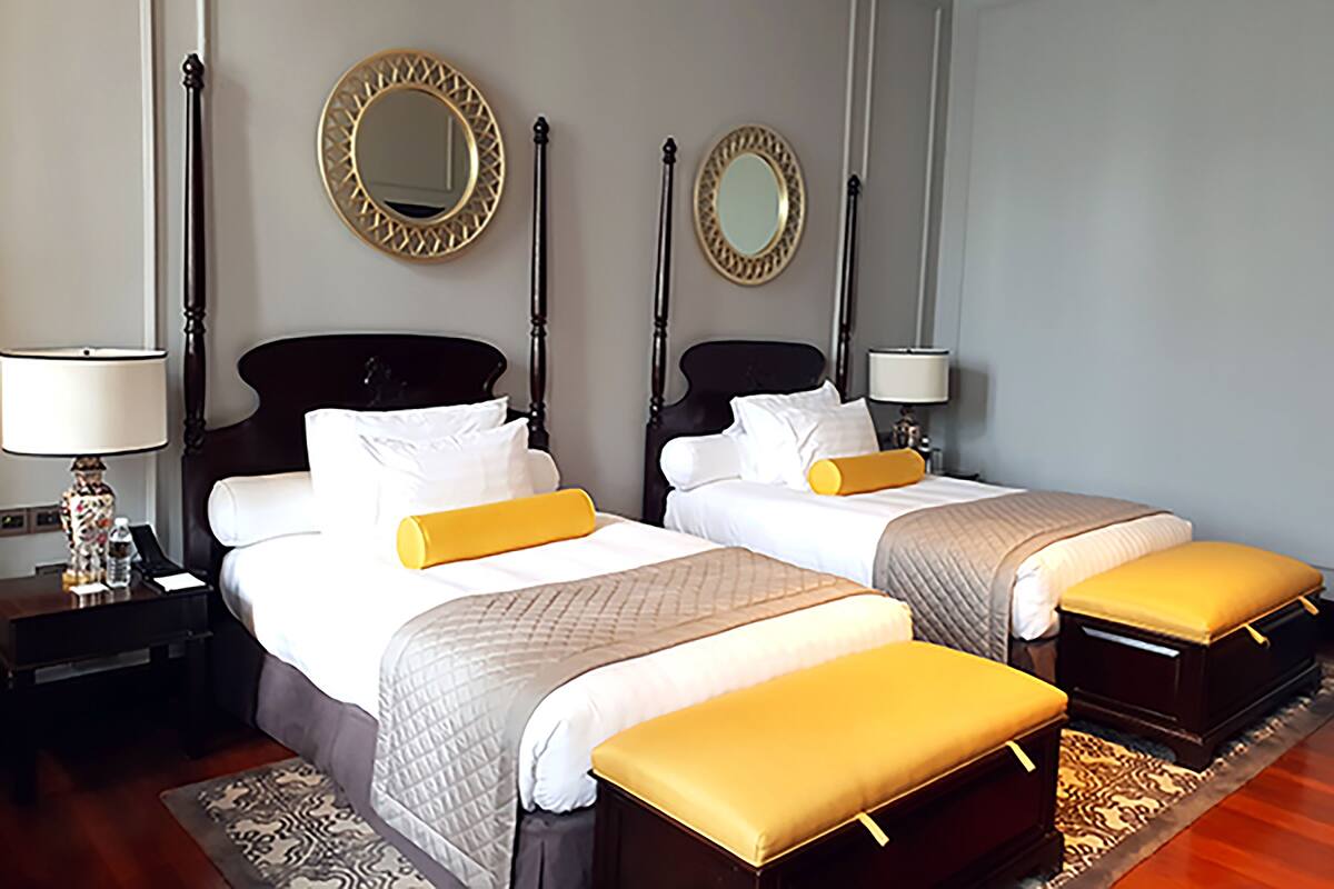A hotel room with two beds, a nightstand, a lamp, and a mirror on the wall.