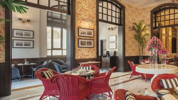 Un vestíbulo de hotel con muebles de mimbre rojo, cuadros enmarcados en las paredes y un ventanal grande.
