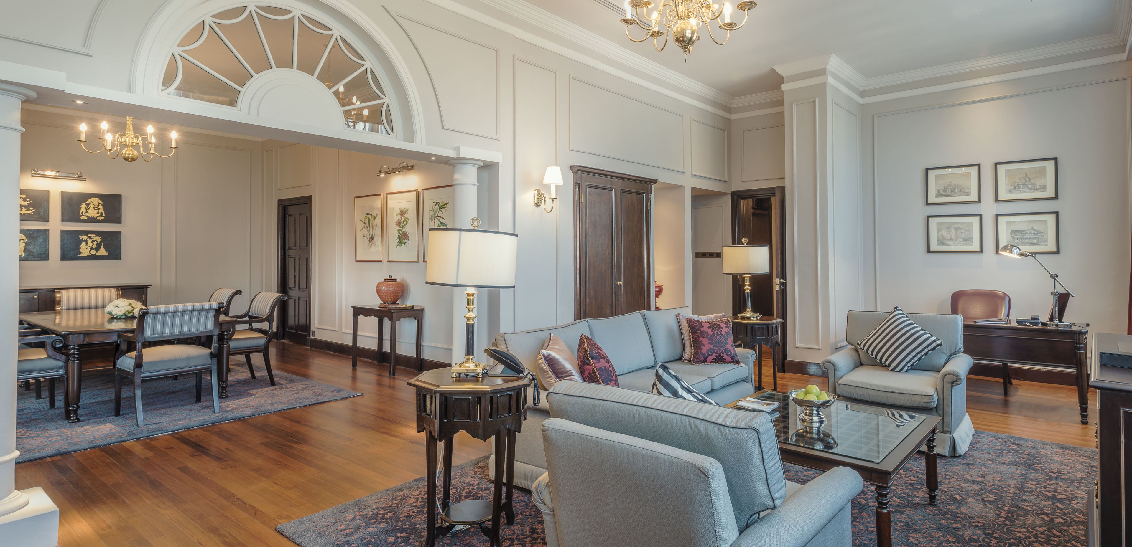 A spacious living room with a dining area, featuring a chandelier, framed artwork, and a large window.