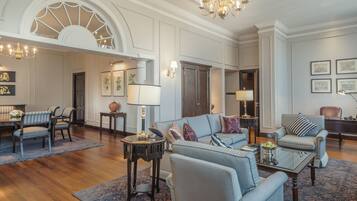 A spacious living room with a dining area, featuring a chandelier, framed artwork, and a large window.