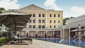 A pool area with lounge chairs and umbrellas, a large building with a lion emblem, and a clear sky. - The Strand Yangon (Yangon)
