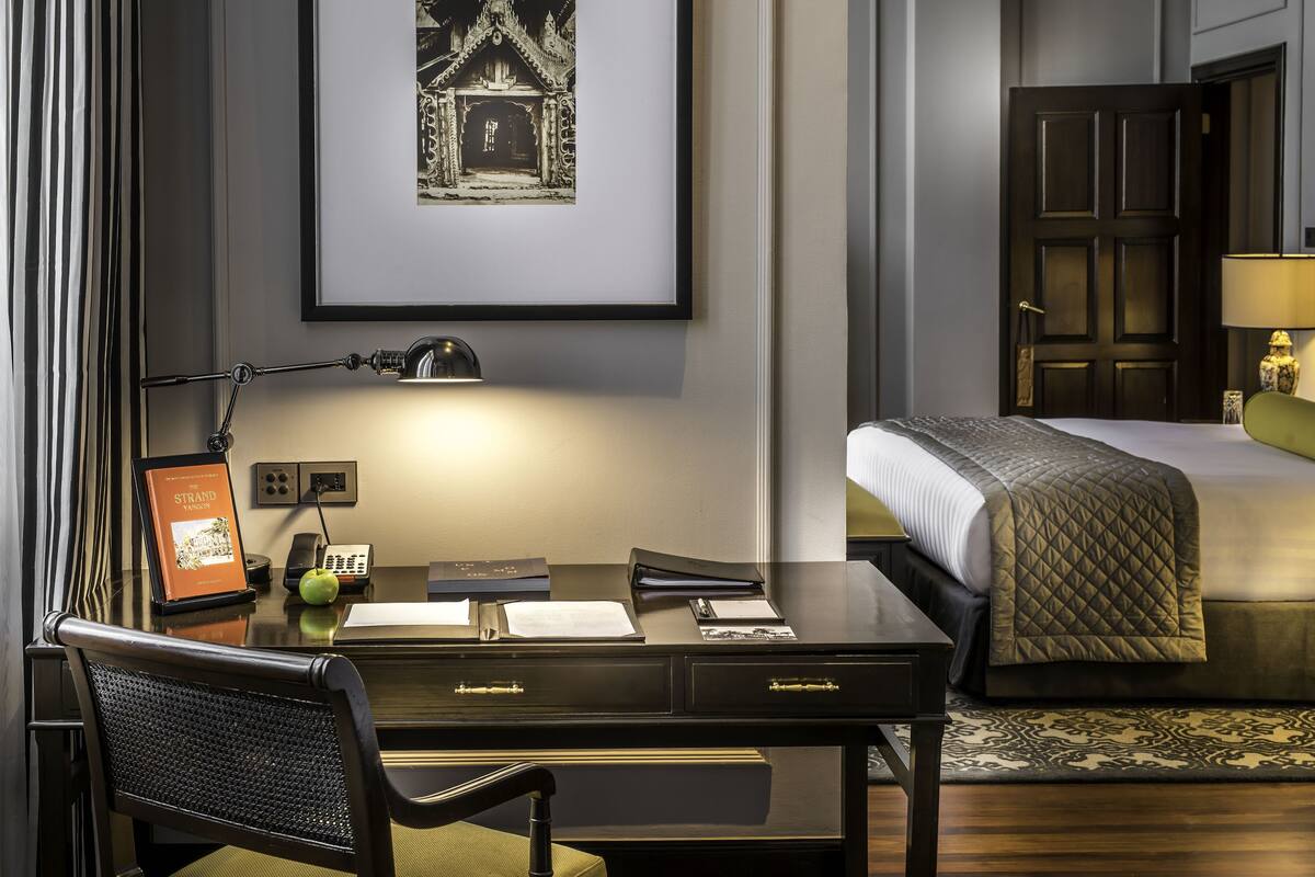 A hotel room with a desk, chair, bed, and a framed picture on the wall.