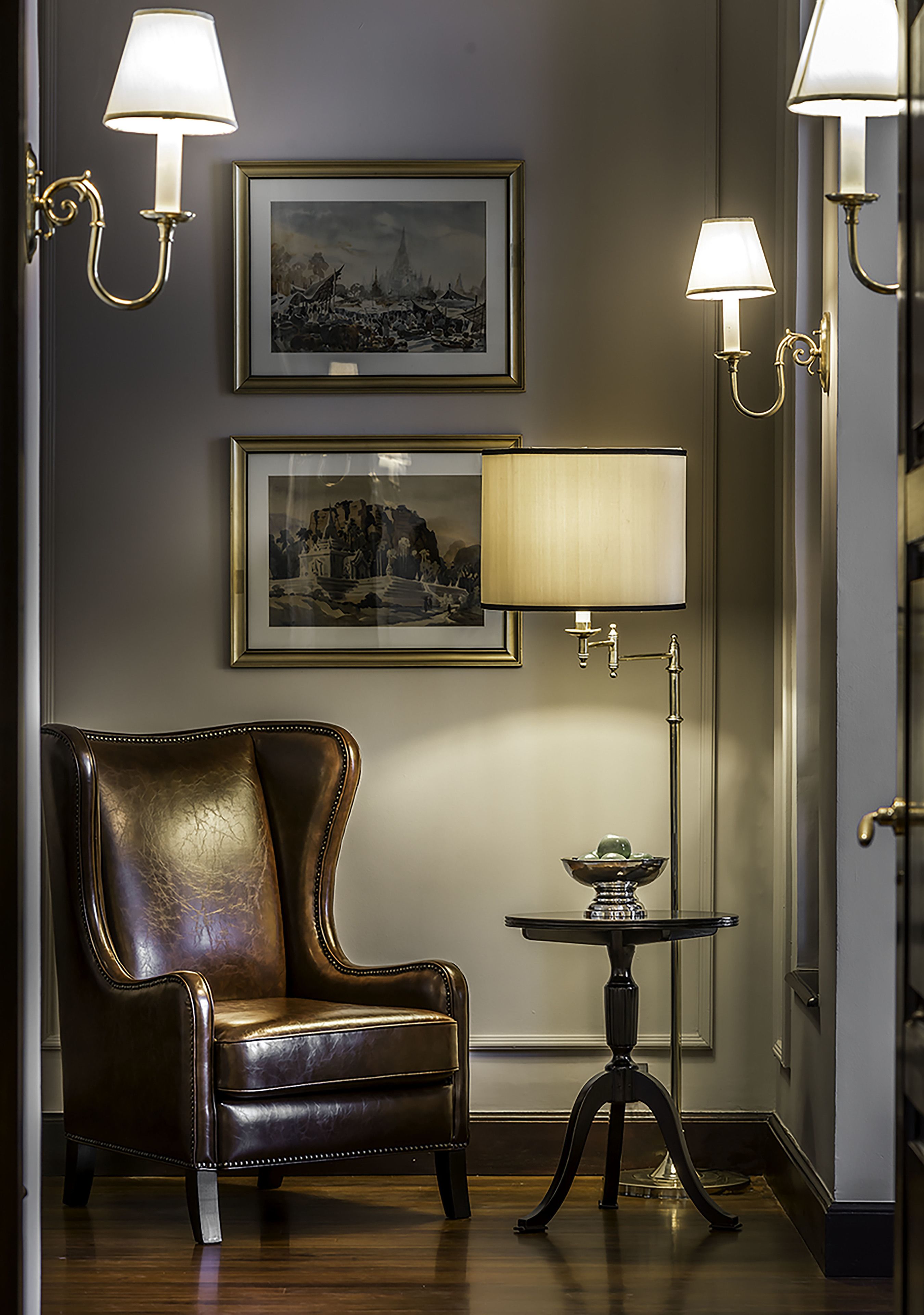 Una habitación con un sillón de cuero, una mesa con lámpara y dos cuadros en la pared.