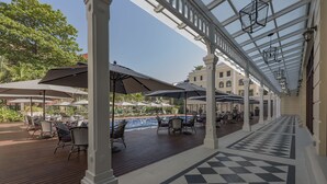 An outdoor patio area with wooden flooring, outdoor seating, and umbrellas. - The Strand Yangon (Yangon)
