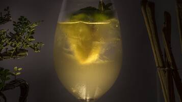 A glass of a clear, yellowish beverage with a garnish, possibly mint, in a stemmed glass.