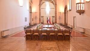 A long banquet table with chairs, flags, and a podium in a room with arched ceilings and wall sconces. - Pousada Castelo de Alcácer do Sal - Historic Hotel (Alcacer do Sal)