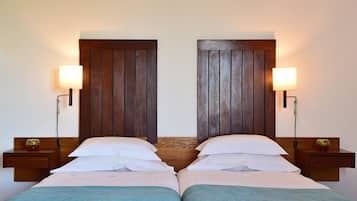 Una cama doble con sábanas blancas y un edredón azul, flanqueada por cabeceros y mesitas de noche de madera con lámparas.