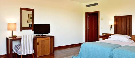 Una habitación de hotel con cama, televisión, escritorio con lámpara, espejo y armario.