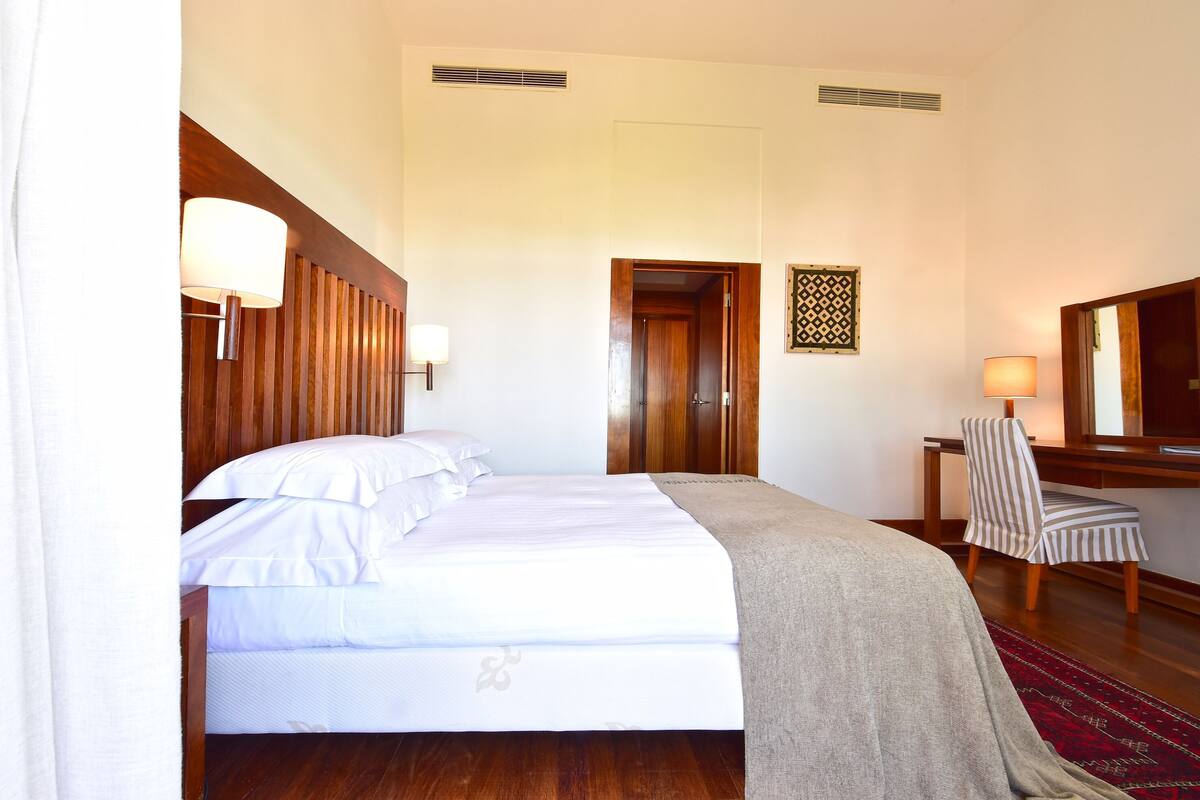 A hotel room with a bed, a desk, a chair, and a mirror.