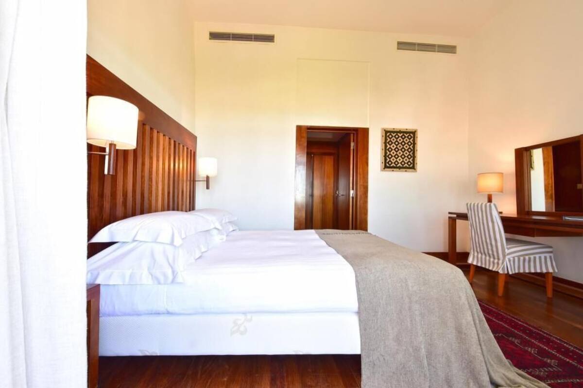 A hotel room with a bed, a chair, a desk, and a mirror.